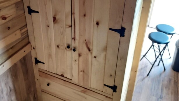 A wooden cabinet with drawers and a door, situated in a room with a wooden floor and a small table with chairs. - Cabin/Farmhouse w/fire pit and wide open spaces (Haslet)