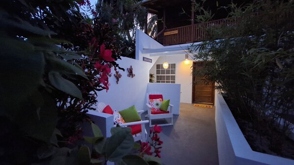A modern outdoor seating area with white walls, a wooden door, and a small window.