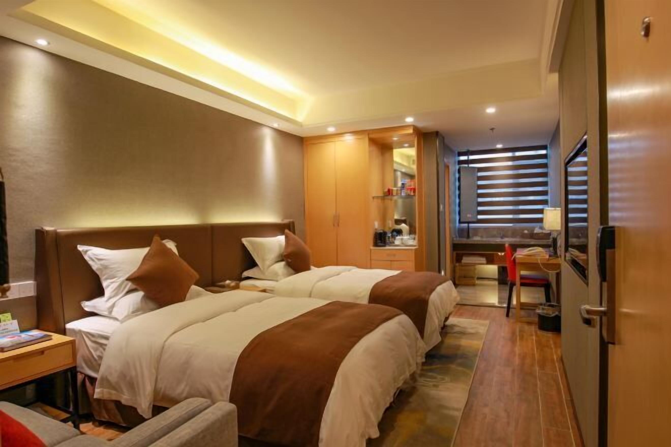 A hotel room with two beds, a desk, a chair, a mirror, and a window with blinds.