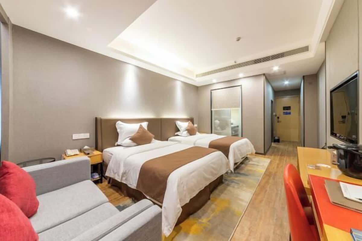 Hotellihuone, jossa on kaksi sänkyä, sohva, televisio ja työpöytä tuolilla.