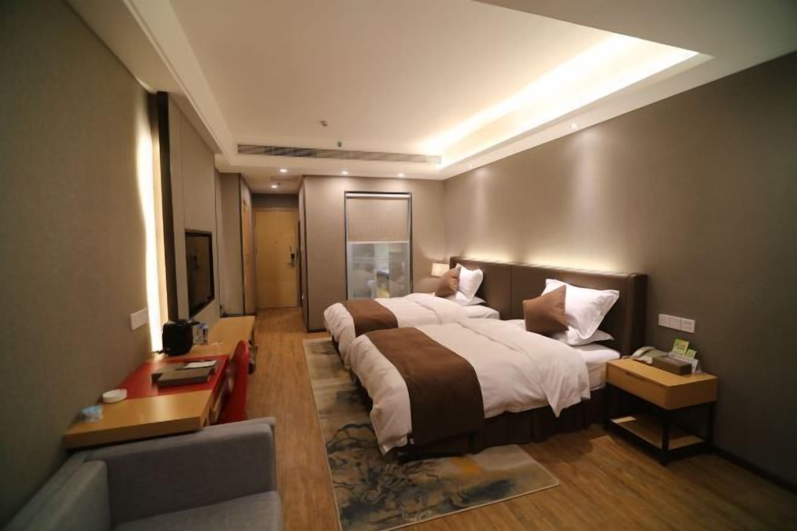 A hotel room with two beds, a desk, a chair, and a small table.
