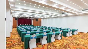 A conference room with rows of tables, a patterned carpet, and a stage with curtains.
