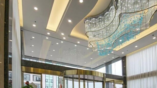 A modern hotel lobby with a curved glass entrance, recessed ceiling lights, and a decorative metal chandelier. - Yong'anzhou Hotel (Mengshan)