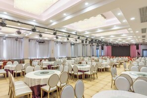Une salle de banquet avec des tables et des chaises rondes, une scène et des rideaux.