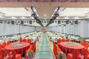 A banquet hall with rows of round tables, each with a red tablecloth and white chairs, arranged for a formal event.