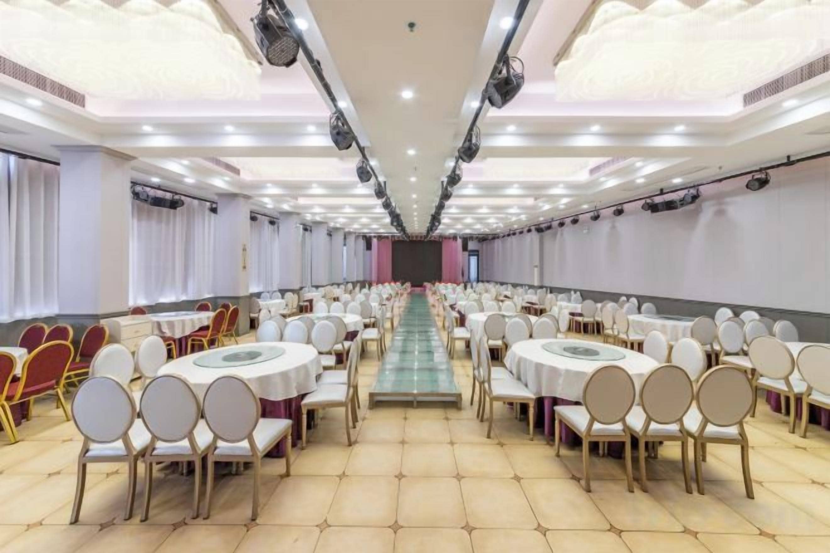 Una sala de banquet amb taules i cadires rodones, un passadís central i una taula llarga al davant.