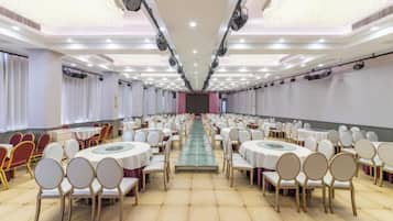 Una sala de banquet amb taules i cadires rodones, un passadís central i una taula llarga al davant.