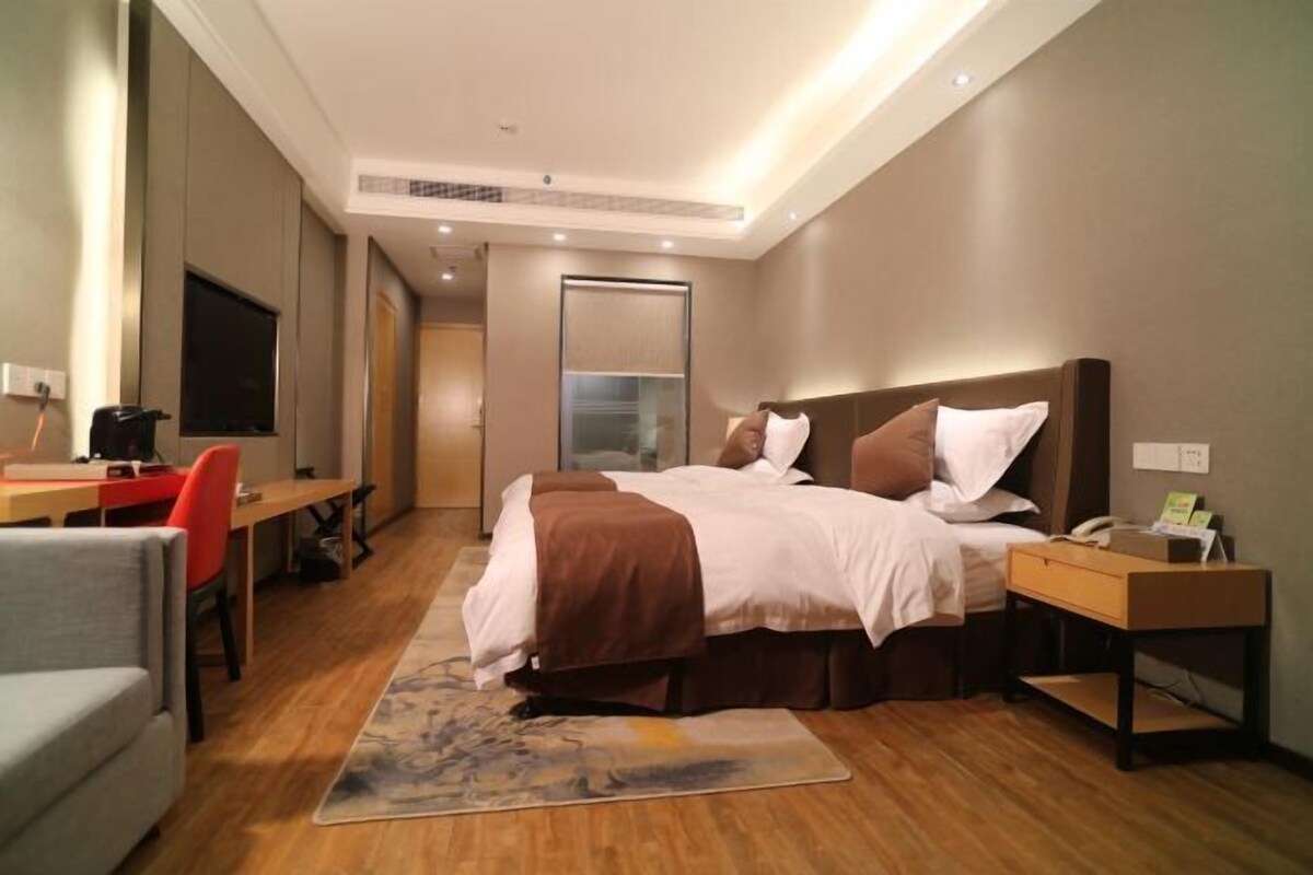 Een moderne hotelkamer met een bed, nachtkastje, bureau, stoel en een televisie.