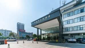 A modern hotel entrance with a clear glass facade, a covered entrance area, and a parking lot with several cars. - Yong'anzhou Hotel (Mengshan)