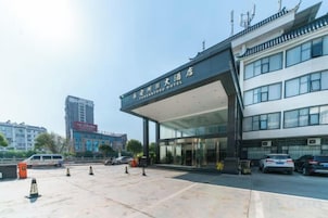 Entrada de hotel con una galería techada, puertas de cristal y un estacionamiento con vehículos.