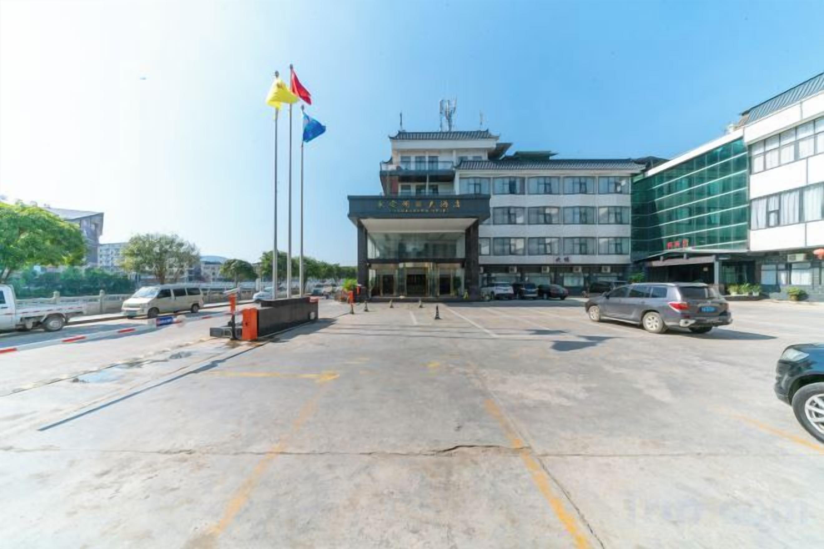 A hotel entrance with a parking lot, a flag, and a building with multiple floors.