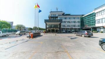 A hotel entrance with a parking lot, a flag, and a building with multiple floors.