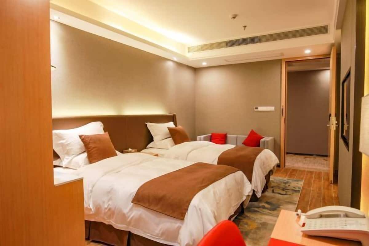 Hotellihuone, jossa on kaksi sänkyä, työpöytä puhelimineen ja ovi, joka johtaa toiseen huoneeseen.