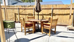 A patio with a round wooden table and four chairs, a hanging umbrella, and a green grill.