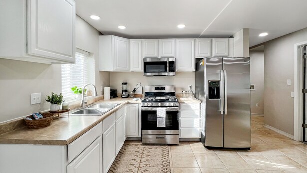 A modern kitchen with white cabinets, stainless steel appliances, and a patterned rug.