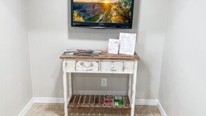 A room with a television mounted on the wall, a wooden console table with papers and a magazine, and a tiled floor.