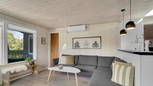 Un salon moderne avec un canapé d’angle gris, une table basse blanche et une grande fenêtre donnant sur un paysage verdoyant.