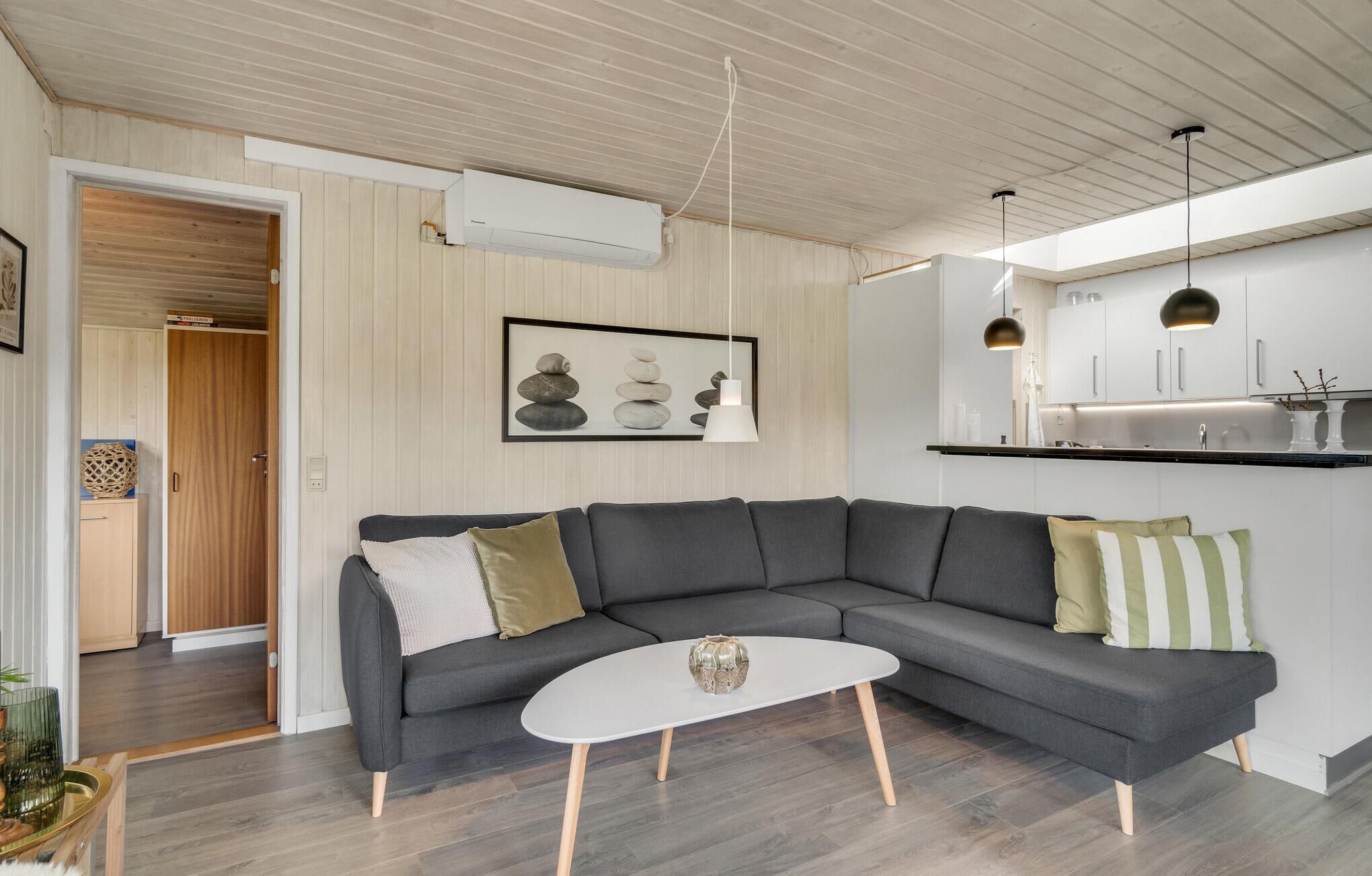 Een moderne woonkamer met een grijze modulaire bank, een witte salontafel, en een keuken met witte kasten en hanglampen.