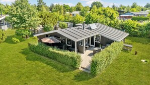 Une maison moderne dotée d’un patio couvert, entourée d’une végétation luxuriante et d’autres maisons.