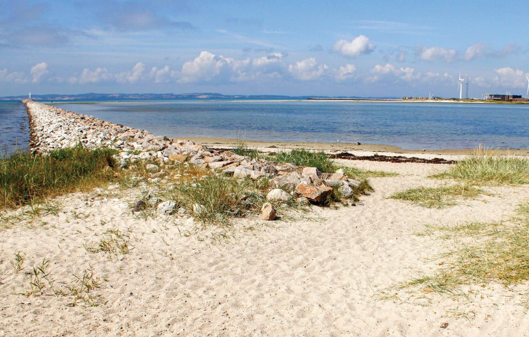 Een kustlandschap met een rotsen rijk gebouwd breekwater, een zandstrand en een kalme zee.