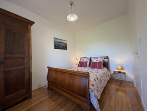 A bedroom with a wooden bed, a nightstand with a lamp, a wooden wardrobe, and a wall-mounted picture.