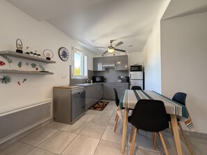 Ett kompakt kök med moderna apparater, en matplats med bord och stolar samt dekorativ väggkonst.
