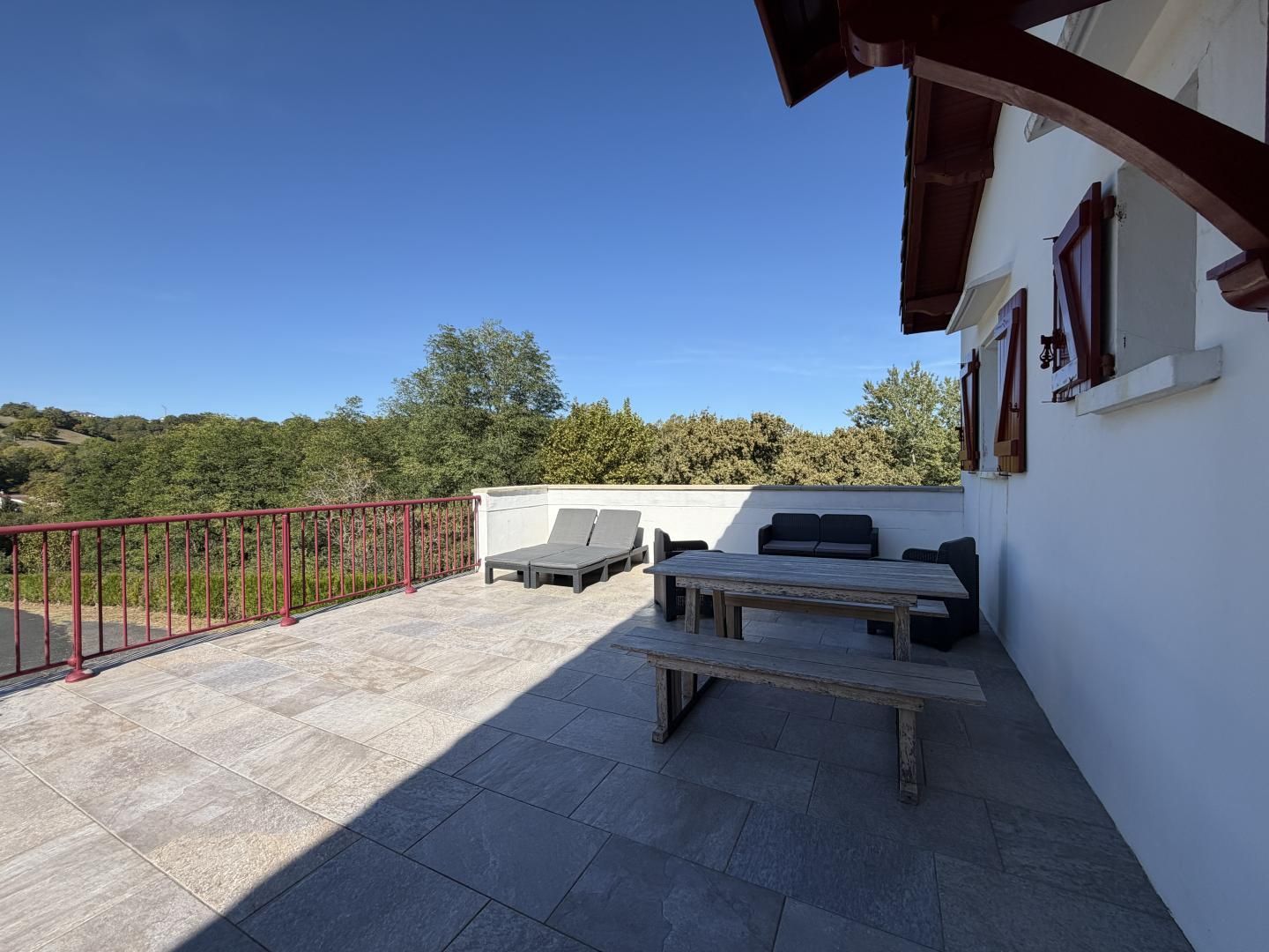 Una terraza en la azotea con barandilla roja, una mesa y dos sillones de relax.