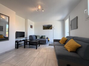 Ett modernt vardagsrum med en grå soffa, ett soffbord, en platt-TV och en golvlampa.