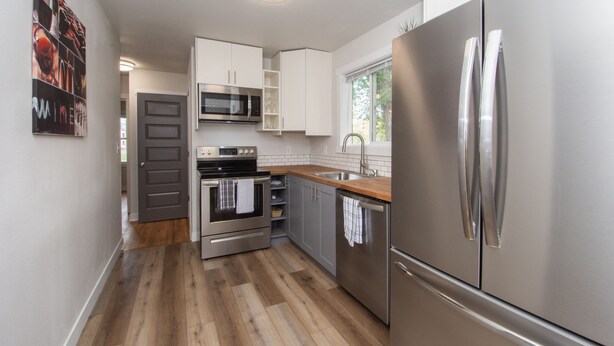 A modern kitchen with stainless steel appliances, white cabinetry, and a wooden floor. - Stylish Home a Block Away from Entertainment (Fargo)