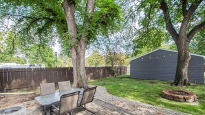 A backyard patio with a table and chairs, surrounded by trees and a shed. - Stylish Home a Block Away from Entertainment (Fargo)