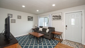 A living room with a sofa, coffee table, and TV. There are wall decorations and a door. - Stylish Home a Block Away from Entertainment (Fargo)