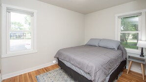 A bedroom with a bed, a nightstand, a lamp, and two windows. - Stylish Home a Block Away from Entertainment (Fargo)