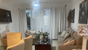 Ein modernes Wohnzimmer mit einer Couch, Sesseln, einem Couchtisch und einem an der Wand befestigten Fernseher.