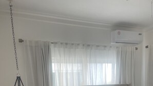 Ein Schlafzimmer mit einem Bett, weißen Vorhängen und einer Klimaanlage.
