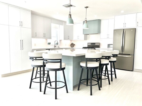 A modern kitchen with white cabinets, a central island with bar stools, stainless steel appliances, and pendant lighting. - Ocean Harmony – your luxurious, peaceful retreat by the Beach (Treasure Cay)