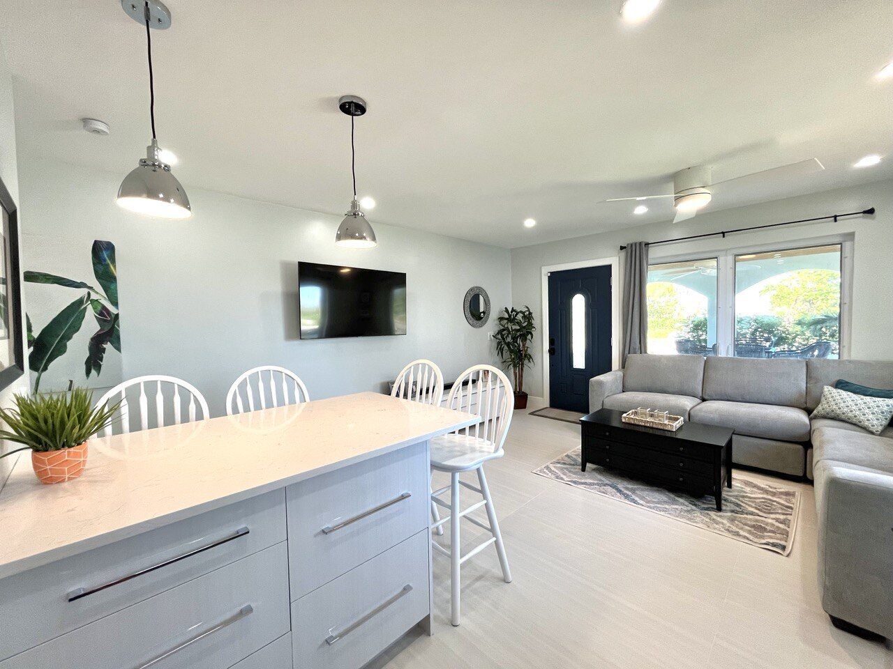 Una sala de estar moderna con un sofá gris, un comedor con sillas blancas y una cocina con una isla grande.
