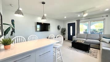 Una sala de estar moderna con un sofá gris, un comedor con sillas blancas y una cocina con una isla grande.