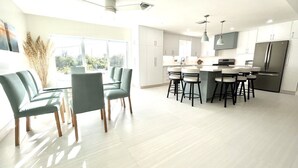 Une cuisine moderne avec des meubles blancs, un réfrigérateur en acier inoxydable et un coin repas comprenant une table et des chaises.