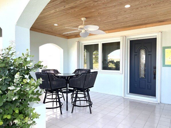 An outdoor patio with a table and chairs, a ceiling fan, and a dark blue door. - Ocean Harmony – your luxurious, peaceful retreat by the Beach (Treasure Cay)