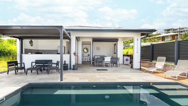 A modern outdoor pool area with a covered patio, lounge chairs, and a dining area. - Romantic Villa Laupie 5 minutes from Case Pilote, a haven of peace (CASE PILOTE)