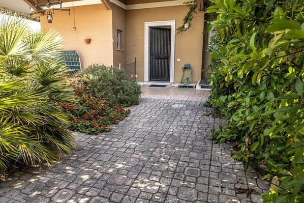 A paved entrance with a door, surrounded by greenery and a small garden.