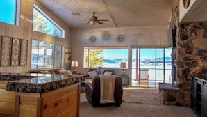 A spacious living area with a stone fireplace, a large window offering a view of the outdoors, and a ceiling fan.