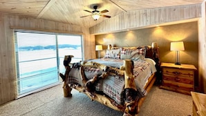 A bedroom with a unique wooden headboard, a bed with plaid bedding, a nightstand with a lamp, and a window with blinds.
