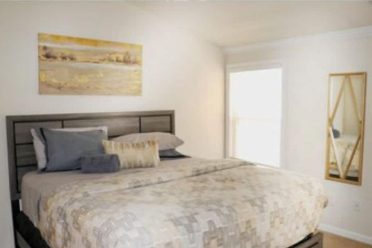 A bedroom with a bed, a painting on the wall, and a mirror.