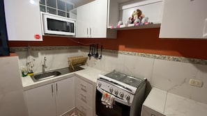 Een keuken met witte kastjes, een magnetron, een fornuis en een spoelbak.