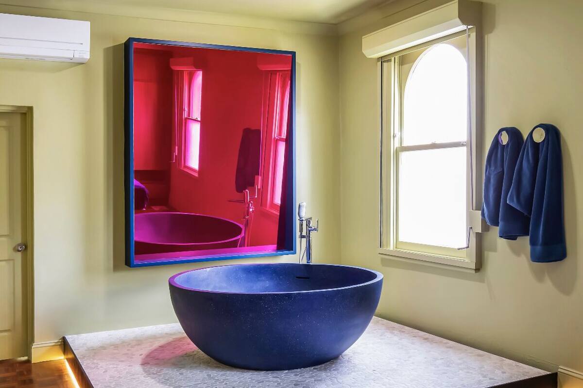 A modern bathroom with a large, round vessel sink, a mirror, and a window with curtains.