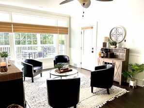 A spacious living room with a large window, a ceiling fan, and a coffee table with decorative items. - Simply Stunning Home in DT Lake Geneva W/Game room! (Lake Geneva)