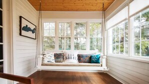 Asiento de balancín de madera con cojines, ventanas amplias y techo de madera.