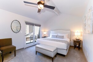 Ein Schlafzimmer mit Bett, Sitzbank, Stuhl, Deckenventilator und einer Tür, die auf einen Balkon führt.