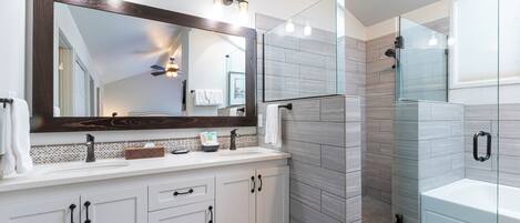 A modern bathroom with a large mirror, a glass shower enclosure, and a bathtub.